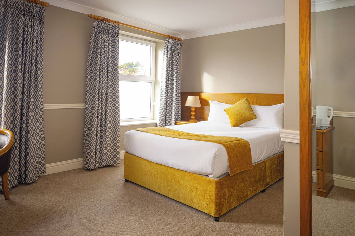 Una habitación de hotel con una cama grande, una mesita de noche con lámpara y cortinas estampadas.