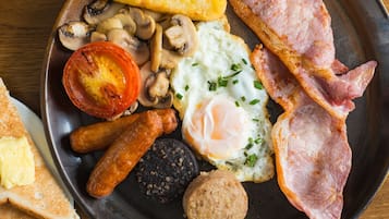Un plato de desayuno con huevos, tocino, salchichas, champiñones, tomate, tostadas y morcilla.