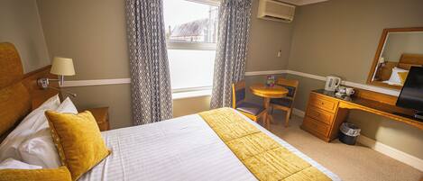 A hotel room with a bed, a desk, a chair, a small table, and a window with curtains.
