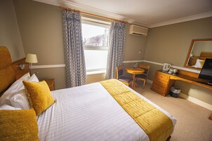 Una habitación de hotel con una cama, un escritorio, una silla, una mesita y una ventana con cortinas.