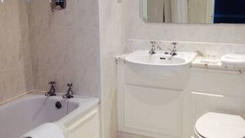 A bathroom with a bathtub, two sinks, a toilet, and a mirror.