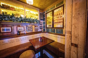 Una zona de bar con un banco de madera, un árbol de Navidad decorado, cuadros en la pared y un tablero con la lista de bebidas.