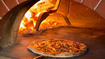 Un horno de pizza con una pizza en su interior, fuego ardiendo y una pared de ladrillo.