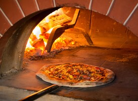 Un horno de pizza con una pizza en su interior, fuego ardiendo y una pared de ladrillo.