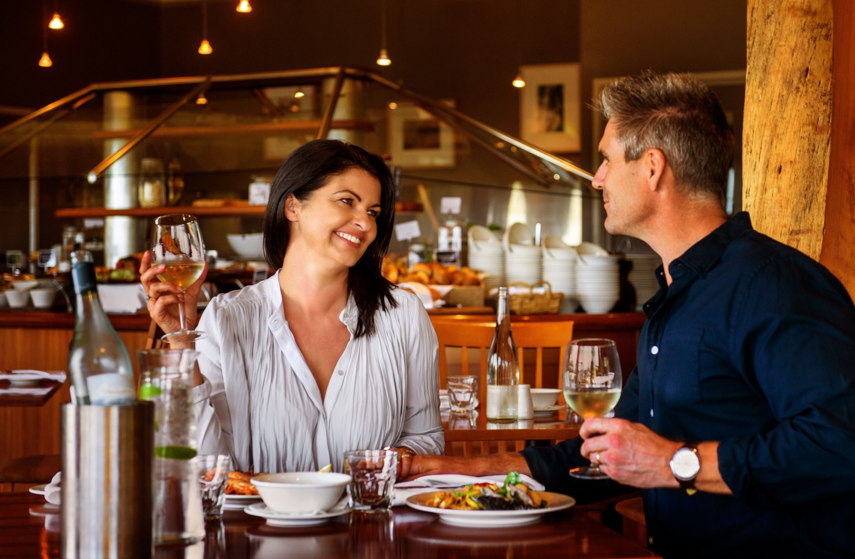 A restaurant with a bar area in the background, a dining table with plates of food, and a bottle of wine.