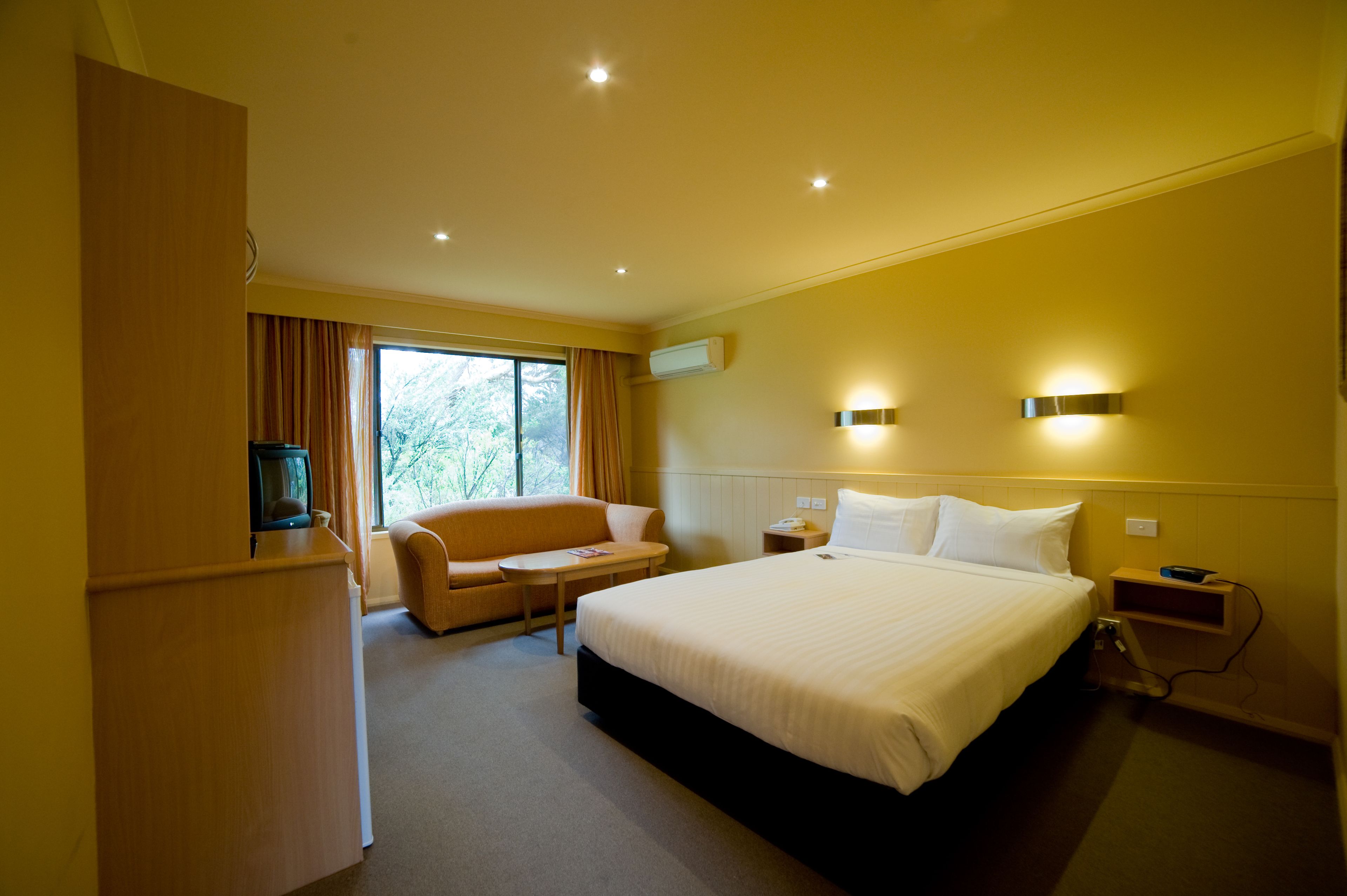 Habitación de hotel con una cama grande, un sofá, una mesita, un televisor y una ventana con cortinas.