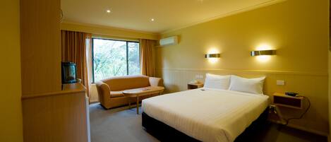 Habitación de hotel con una cama grande, un sofá, una mesita, un televisor y una ventana con cortinas.