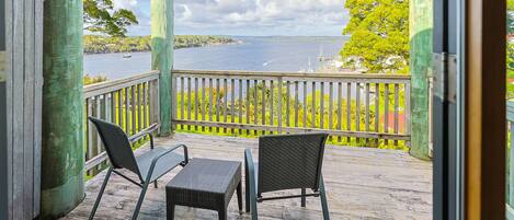 A wooden deck with two chairs and a table, overlooking a body of water and greenery.