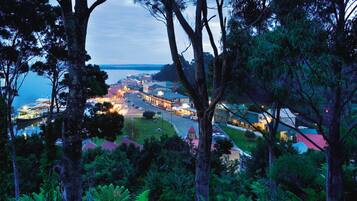 A coastal town at dusk with illuminated buildings, a marina, and surrounding greenery.