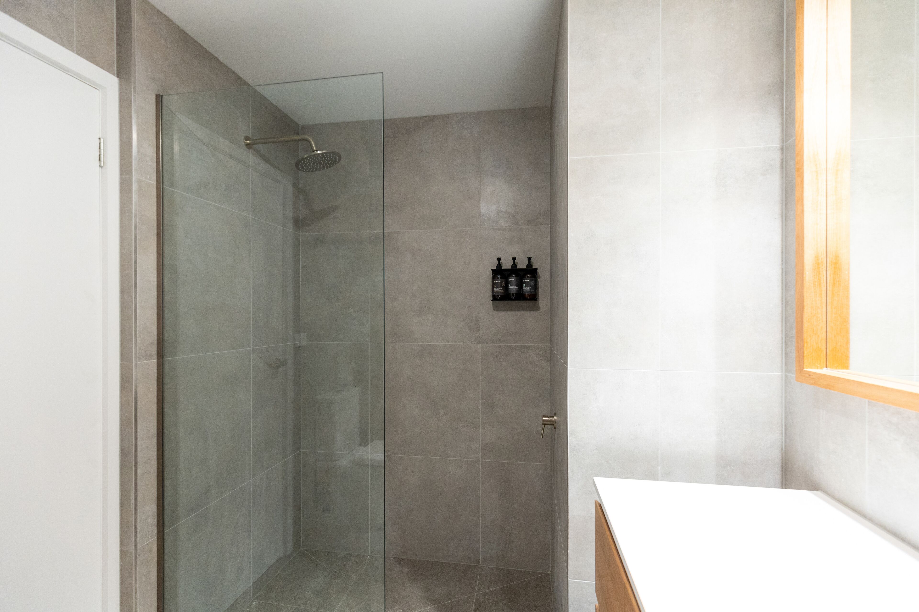 Un baño moderno con ducha de vidrio, lavamanos blanco y mueble de madera.