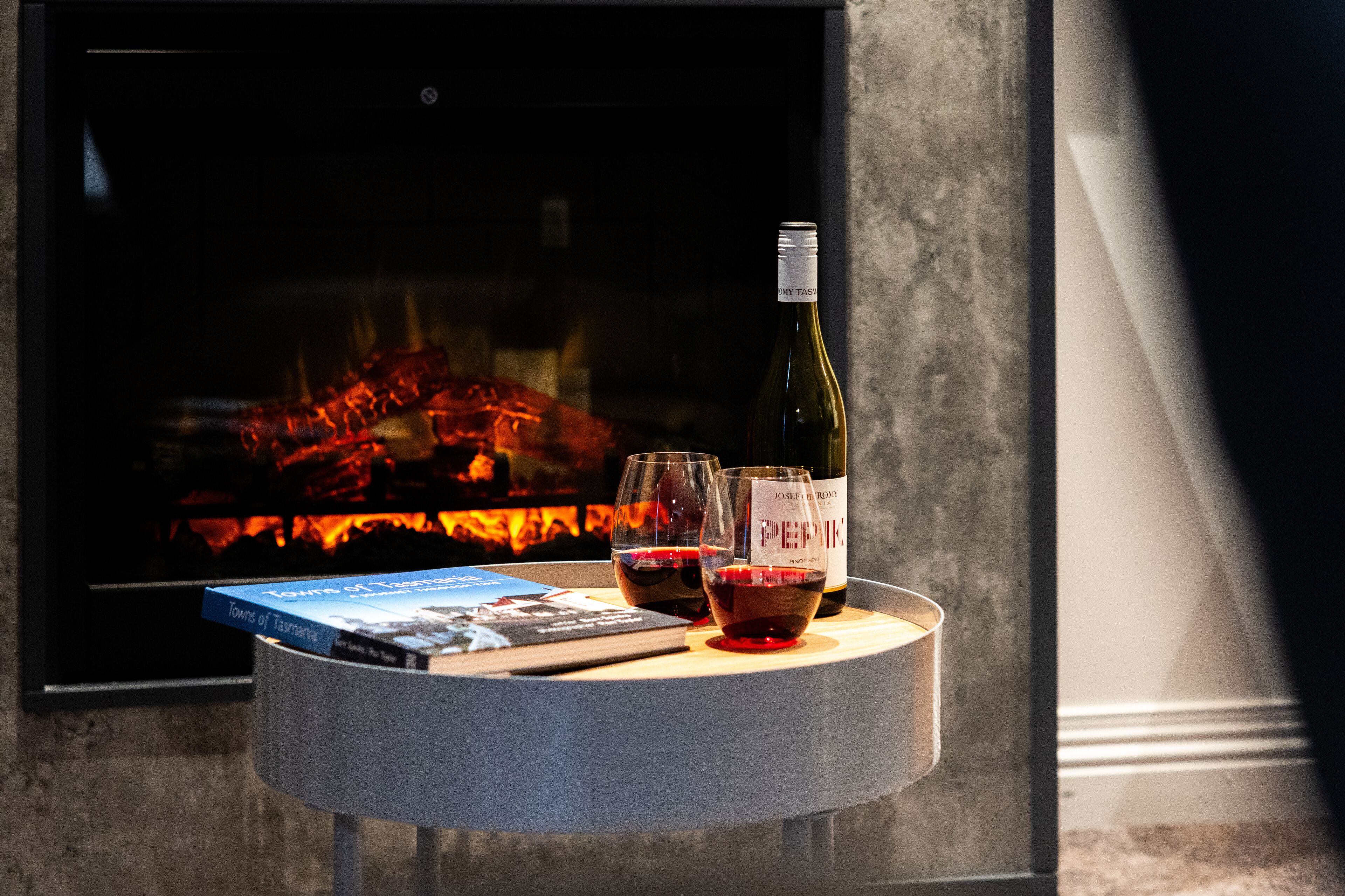 A table with a book titled "Town of Tasmania," two wine glasses, and a bottle of wine in front of a fireplace.