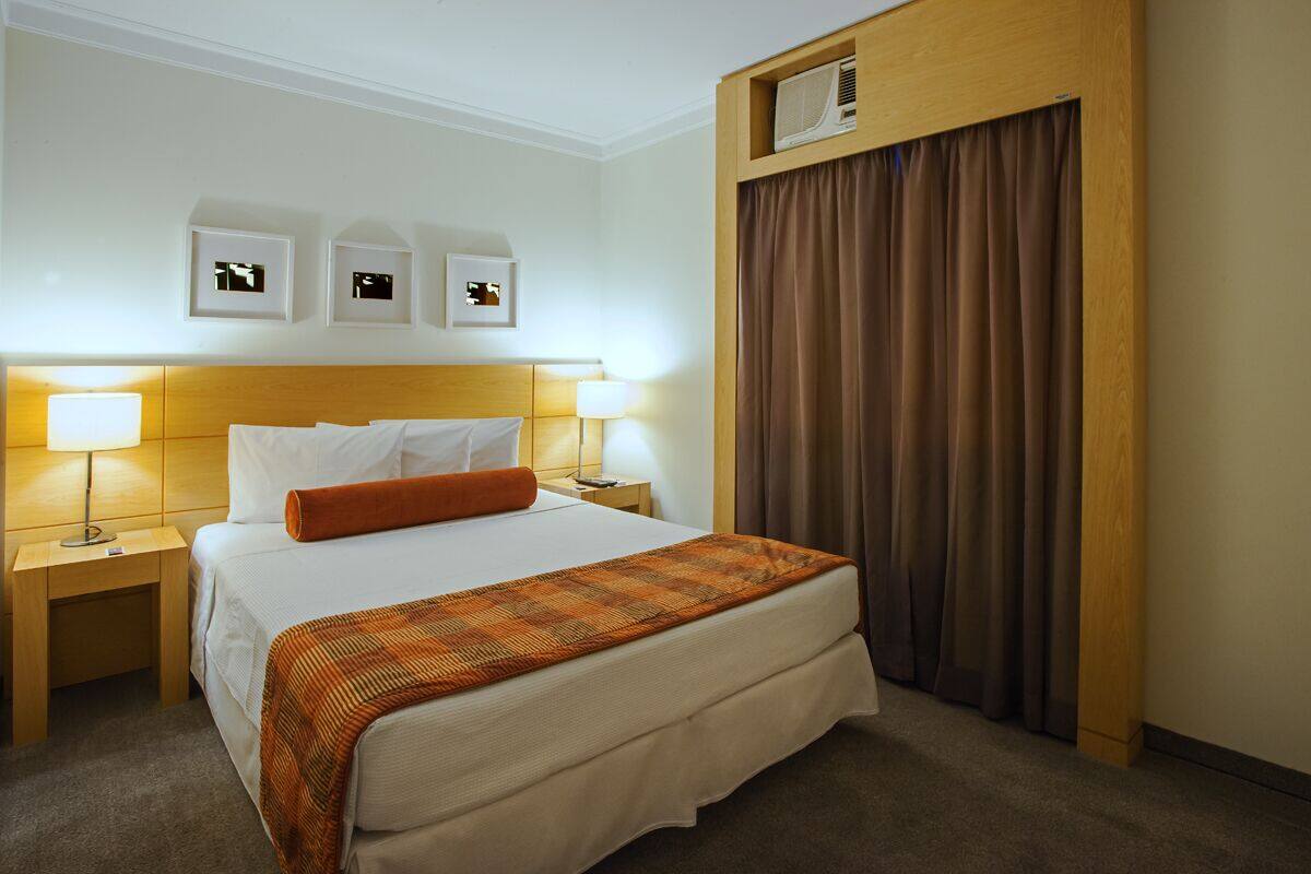 Ein Hotelzimmer mit einem großen Bett, zwei Nachttischlampen, einer Kopfteil und einer Wand-Klimaanlage.