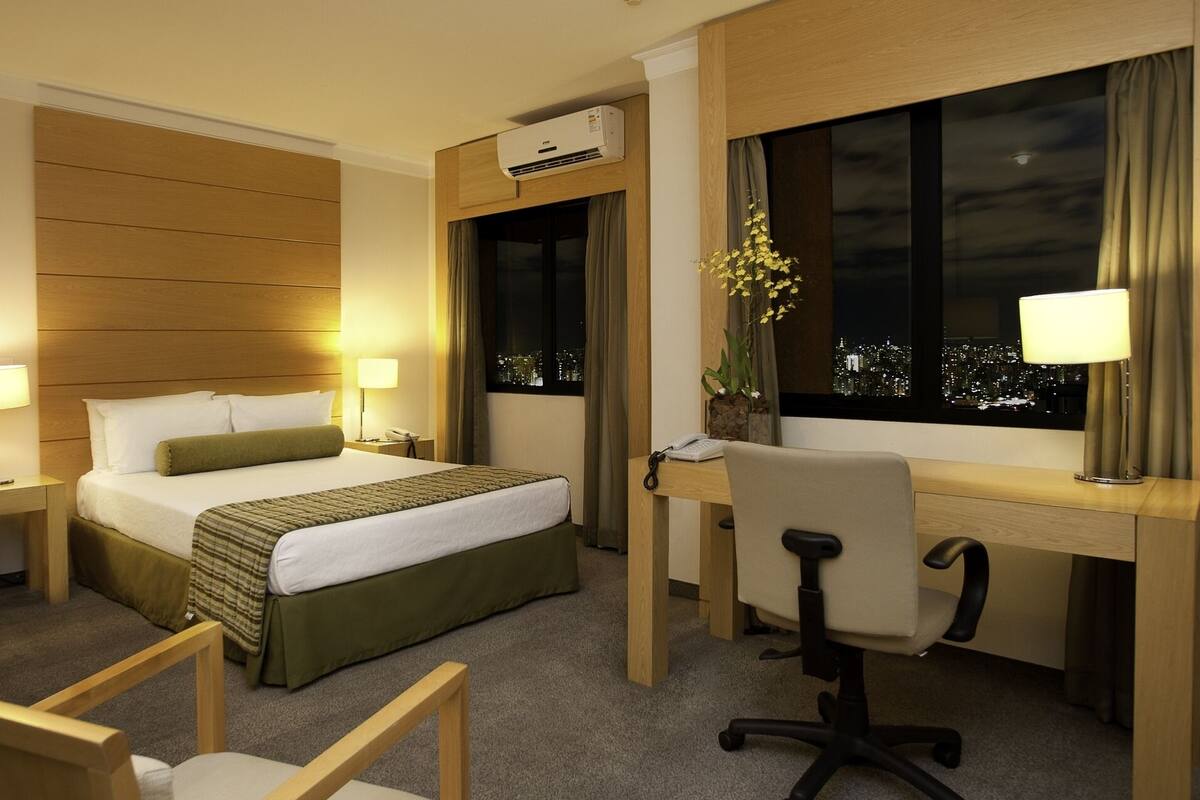 Ein Hotelzimmer mit Bett, Schreibtisch, Stuhl und einem Fenster mit Blick auf die Stadt.