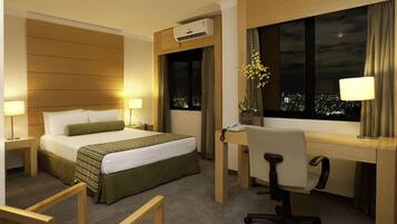 Ein Hotelzimmer mit Bett, Schreibtisch, Stuhl und einem Fenster mit Blick auf die Stadt.