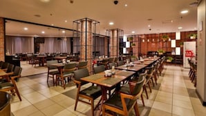 Un restaurante espacioso con varias mesas y sillas, detalles de ladrillo y piso de baldosas.