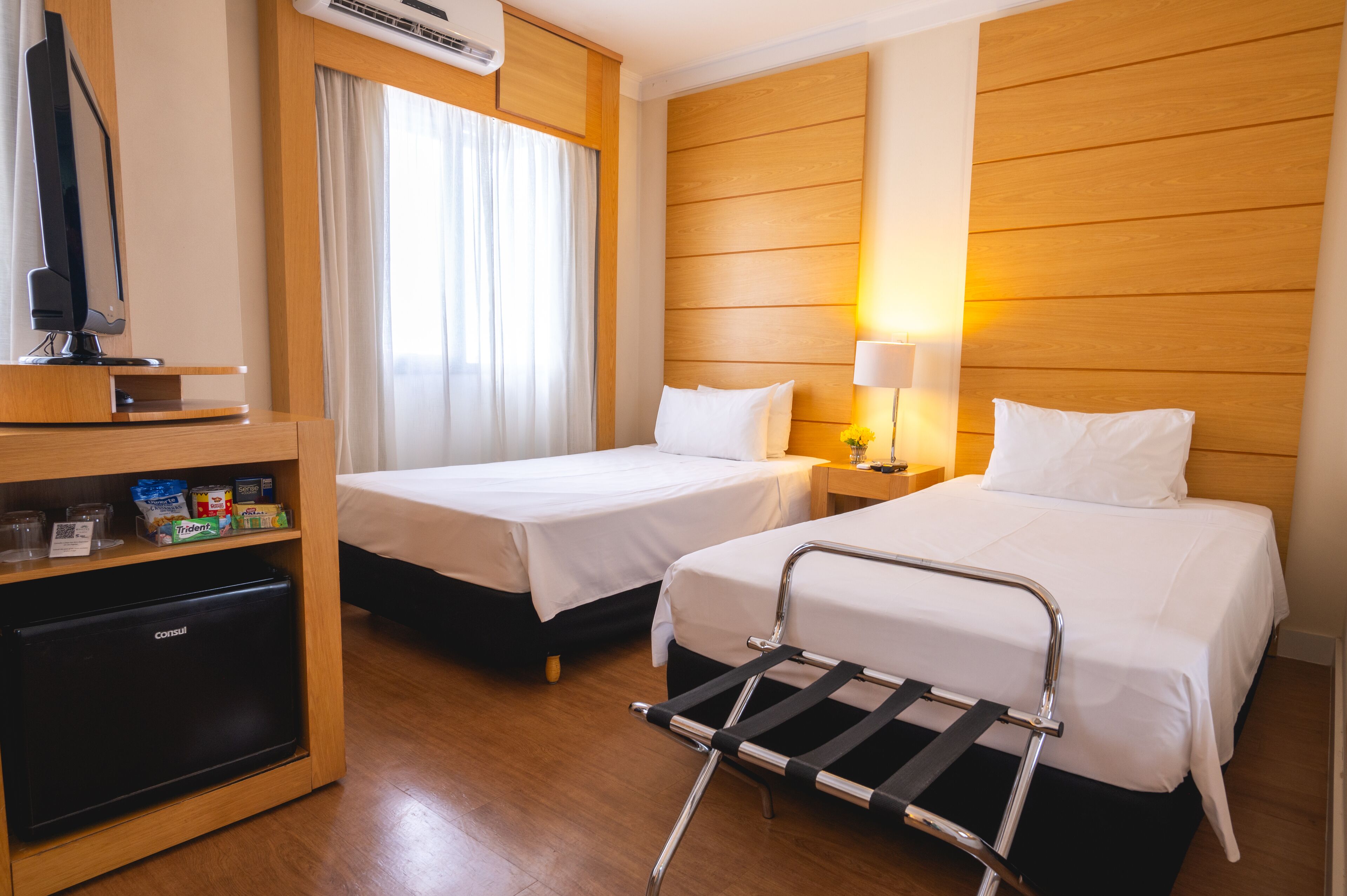 Habitación de hotel con dos camas, televisor, refrigerador pequeño y mesita de noche con lámpara.