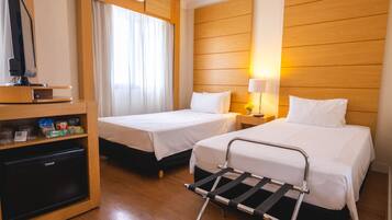 Habitación de hotel con dos camas, televisor, refrigerador pequeño y mesita de noche con lámpara.