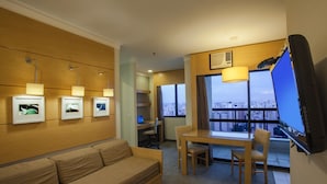 Habitación de hotel con sofá, una mesa de comedor con sillas, televisión y vistas a la ciudad a través de amplias ventanas.