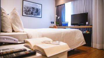 A hotel room with a bed, a desk with a laptop, a television, and a window with curtains.
