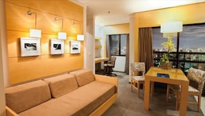 Una habitación de hotel con sofá, una mesa de comedor con sillas, lámpara y cuadros en la pared.