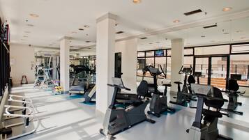 Une salle de sport équipée de divers appareils de cardio, de stations d’entraînement en force et d’un mur recouvert de miroirs.