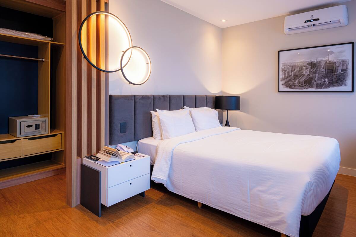 Ein ordentlich eingerichtetes Hotelzimmer mit Bett, Nachttisch und Kleiderschrank.