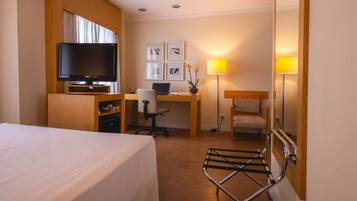 Habitación de hotel con cama, escritorio, computadora, silla, televisor y lámpara.