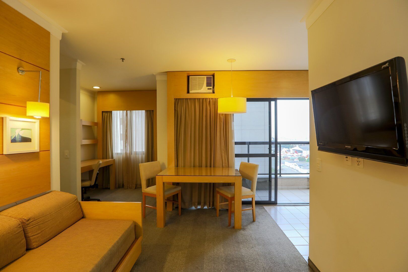 Habitación de hotel con sofá, una mesa de comedor con sillas, televisor y balcón con vistas.