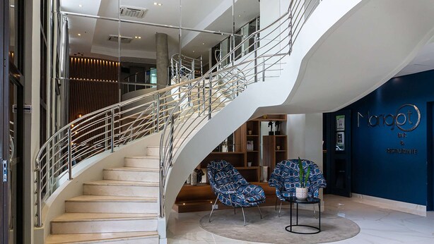 Eine moderne Hotelhalle mit einer geschwungenen Treppe, einer Sitzecke und einer Rezeption.