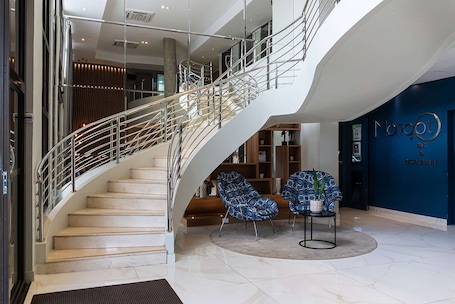 A modern hotel lobby with a curved staircase, seating area, and a reception desk.