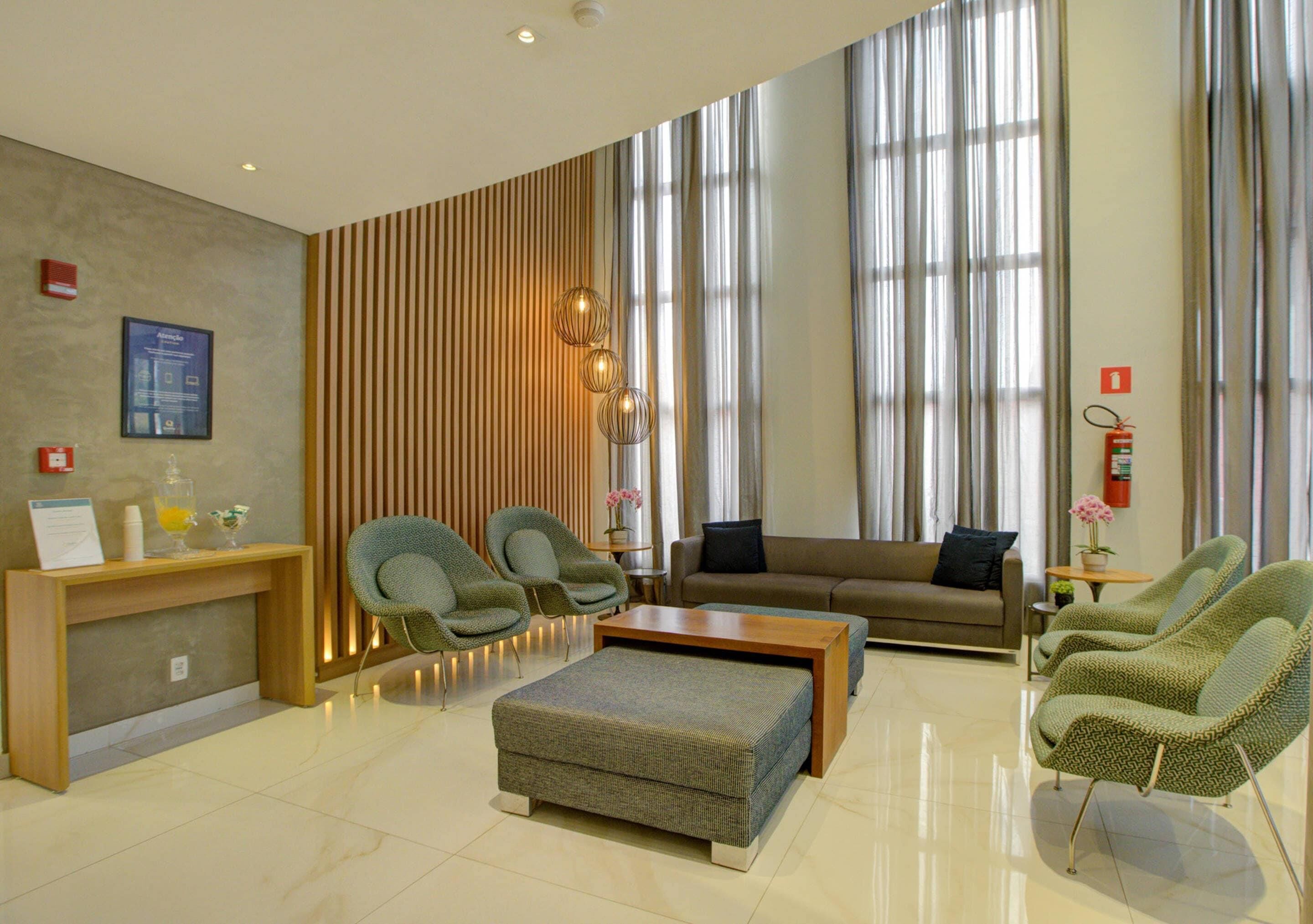 A modern hotel lobby with a reception desk, seating area, and large windows.