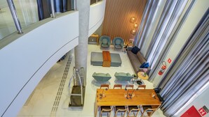 Eine moderne Hotelhalle mit einer zentralen Sitzgelegenheit, einem Holztisch und einer Treppe, die zu einer oberen Ebene führt.