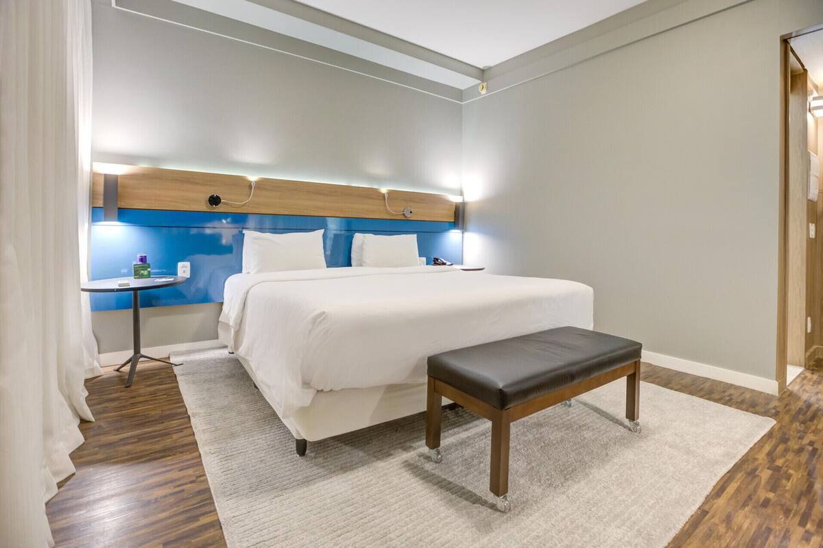 A hotel room with a bed, bedside table, and a bench.