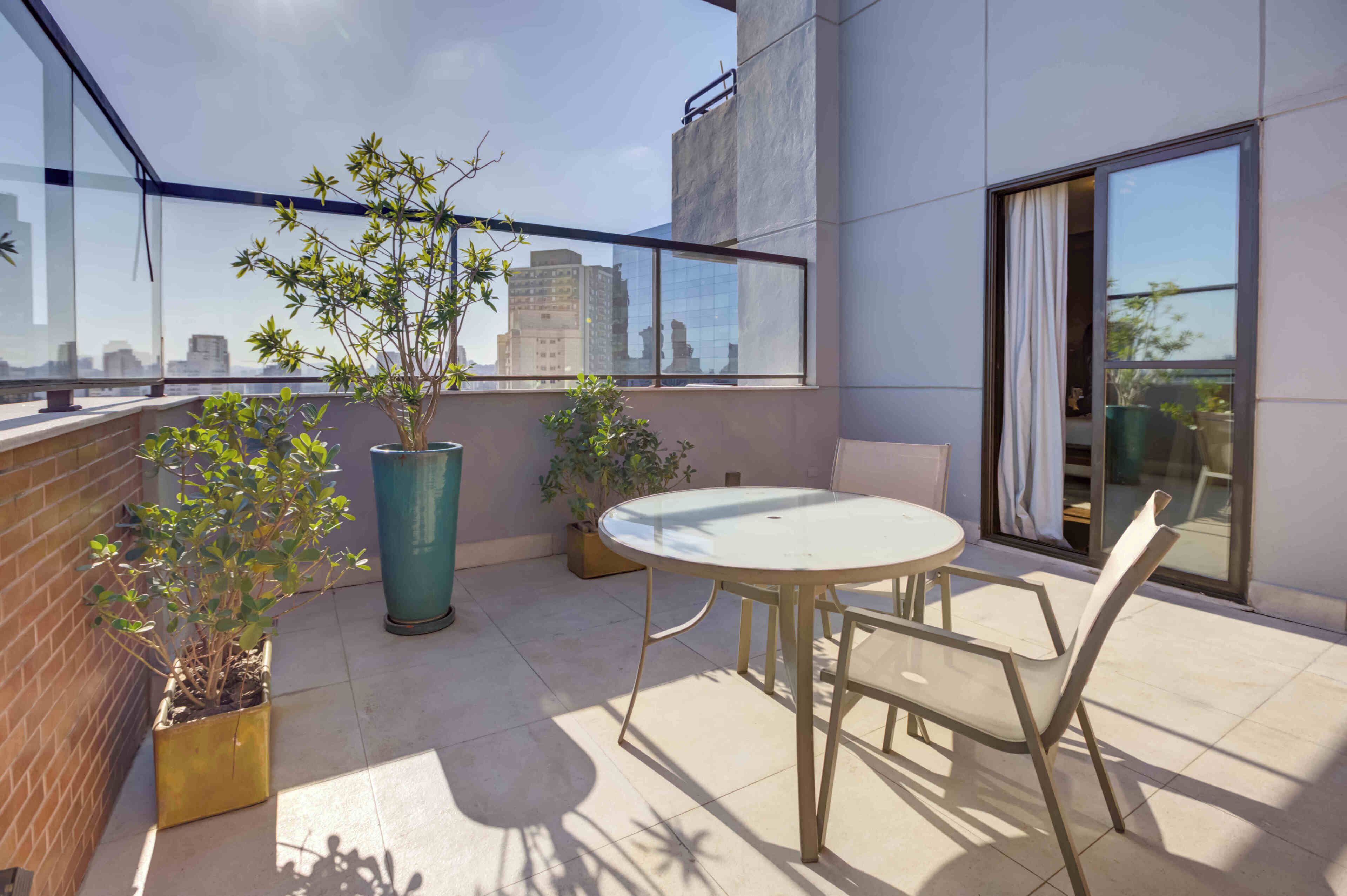 Uma varanda com mesa e cadeiras de vidro, plantas em vasos e vista para o horizonte da cidade.