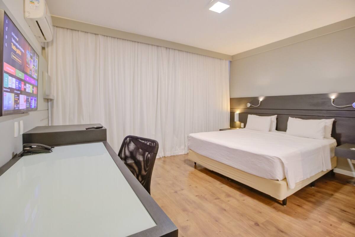 A hotel room with a bed, a desk, and a TV screen displaying a hotel directory.