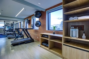 Ein Fitnessraum mit Laufbändern, einer an der Wand befestigten Übungsbälle, einem Wasserspender und Blick auf die Stadt durch große Fenster.