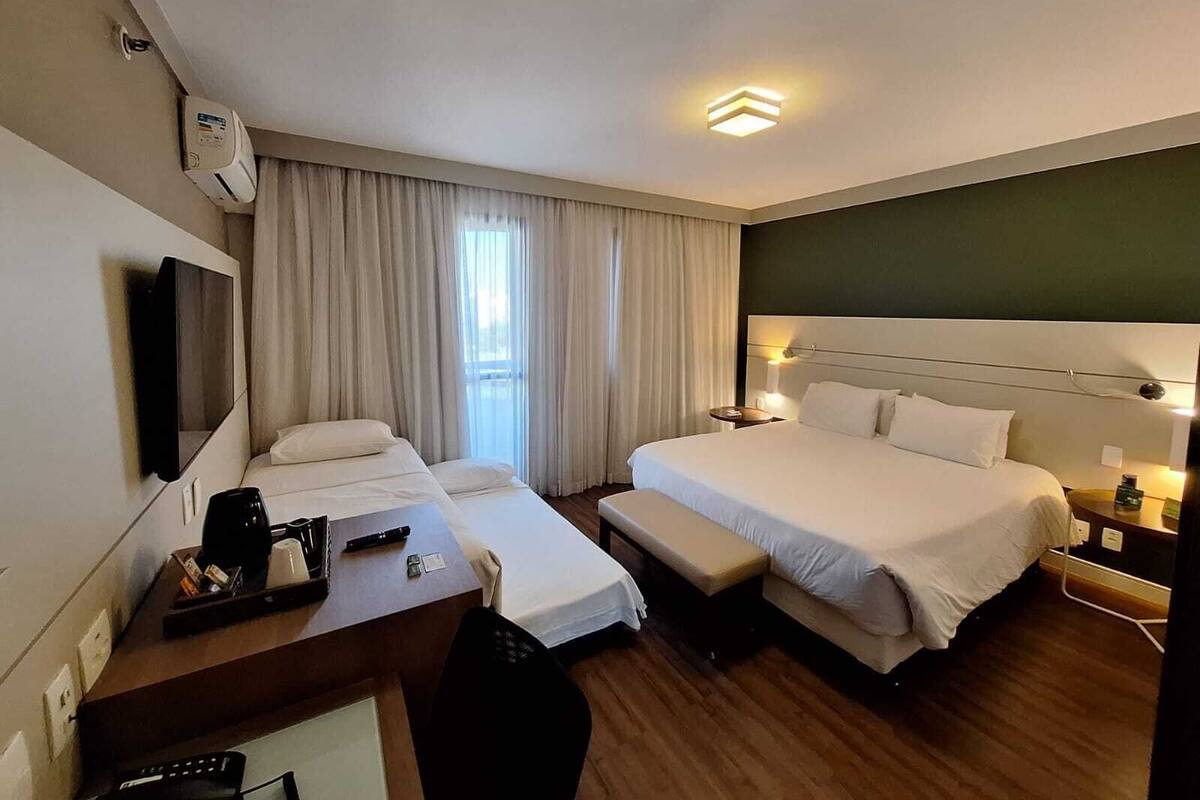 A hotel room with two beds, a desk with a chair, a TV, and a window with curtains.