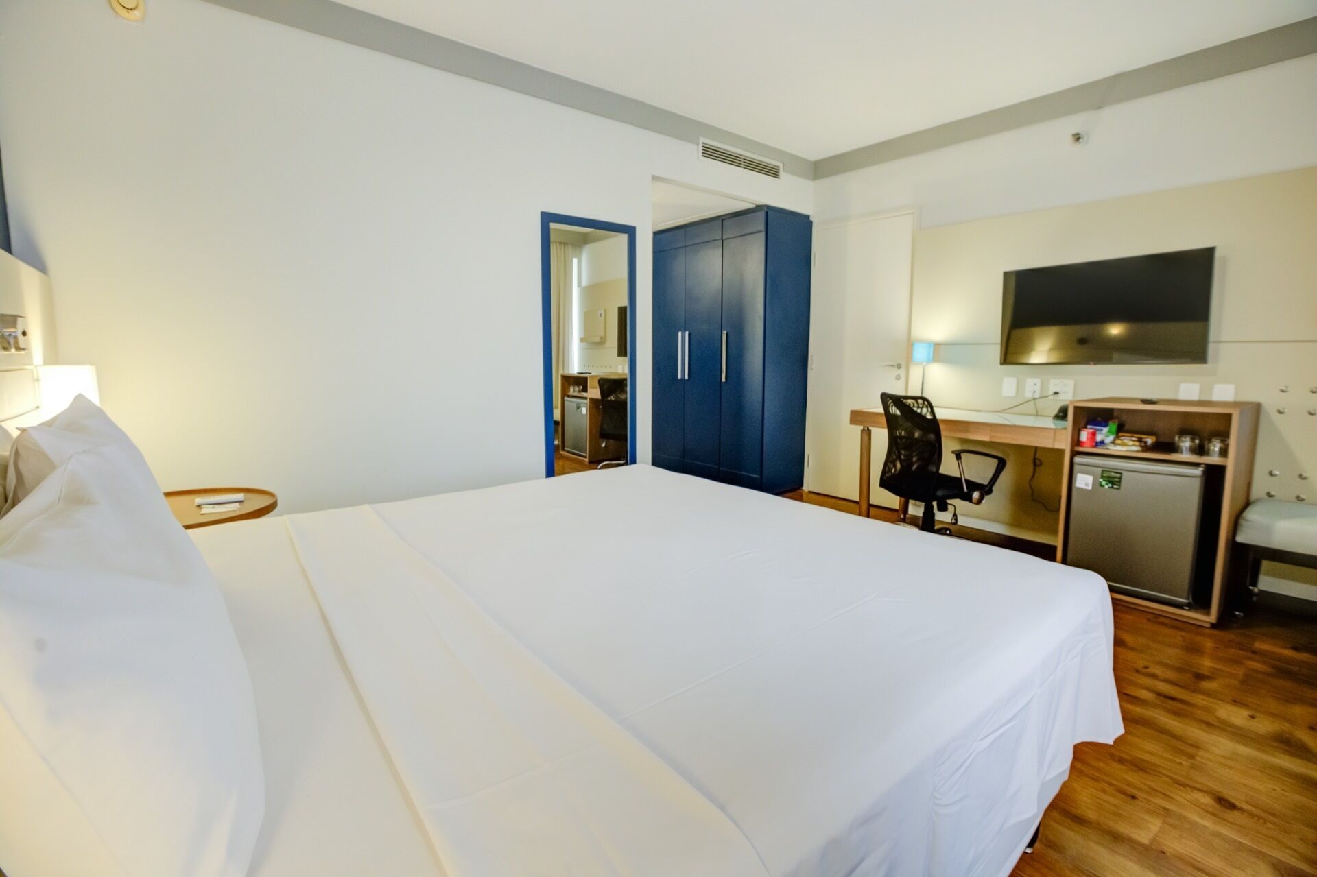 A hotel room with a large bed, a desk with a computer, a TV, and a wardrobe.