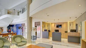 Eine geräumige Lobby mit hoher Decke, einer Treppe und einer Rezeption mit Fernseher.