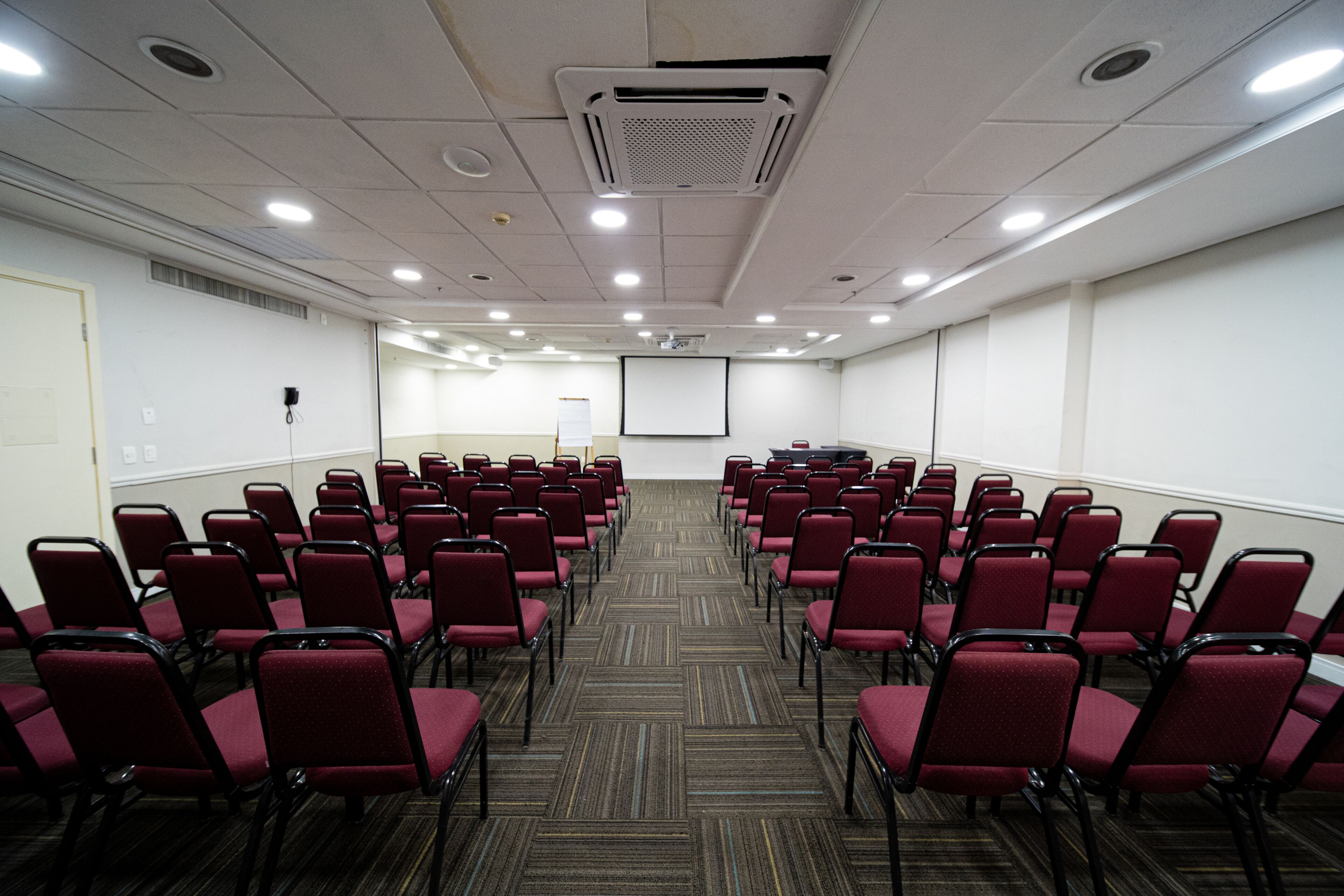 A conference room with rows of red chairs, a projector screen, and a carpeted floor.