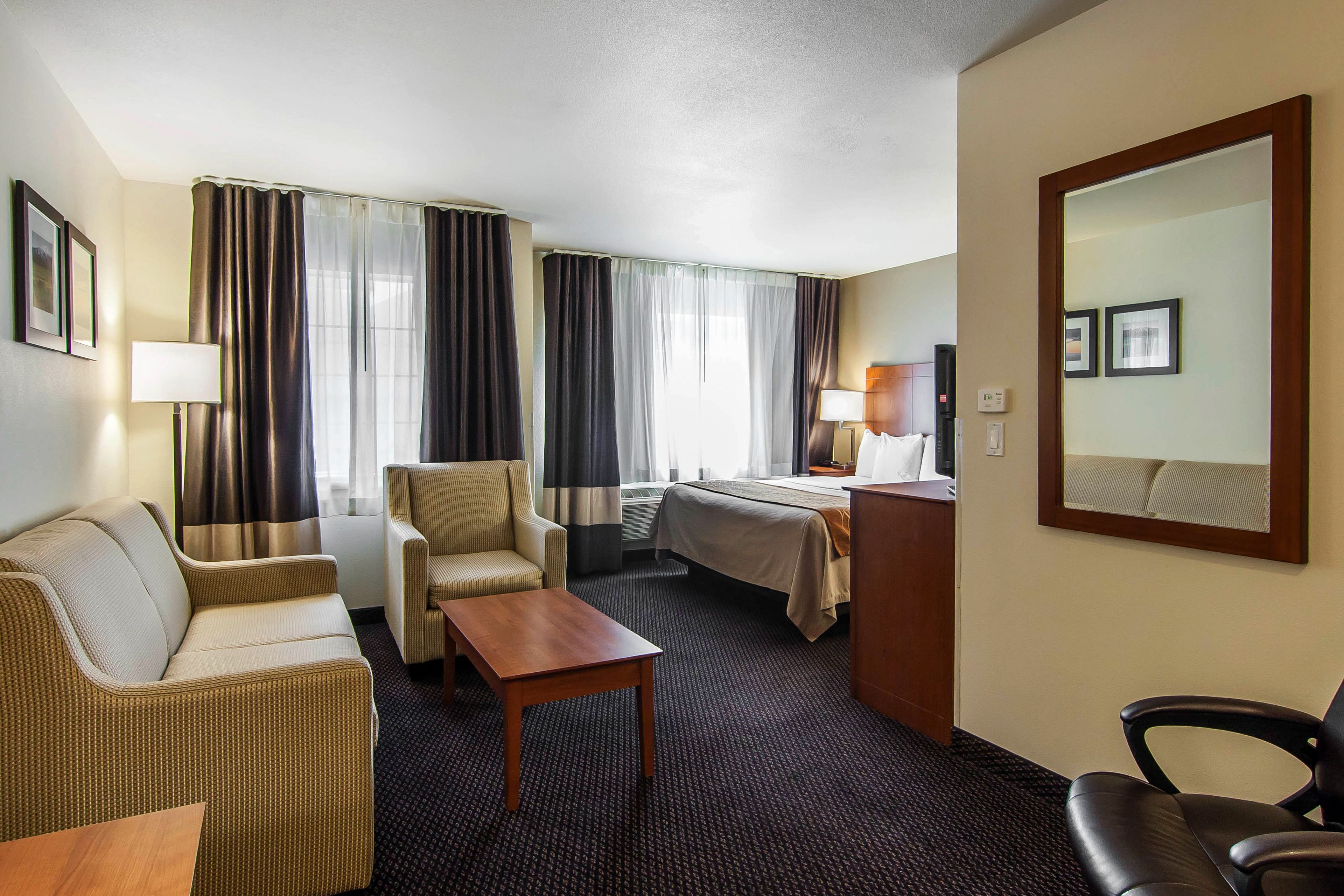 A hotel room with a bed, a sofa, a chair, a desk, and a mirror.