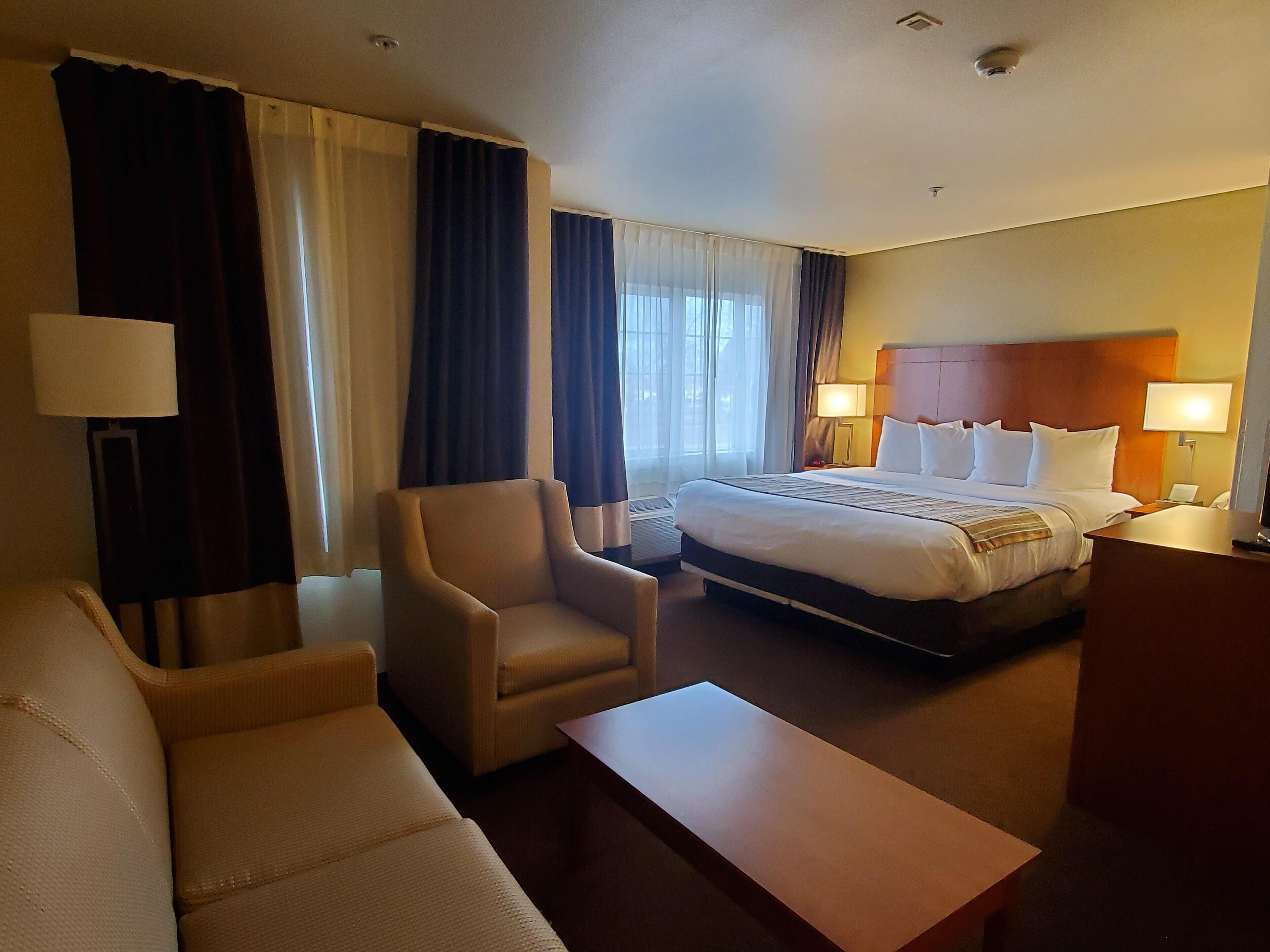 A hotel room with a bed, a sofa, a chair, a desk, and a lamp.