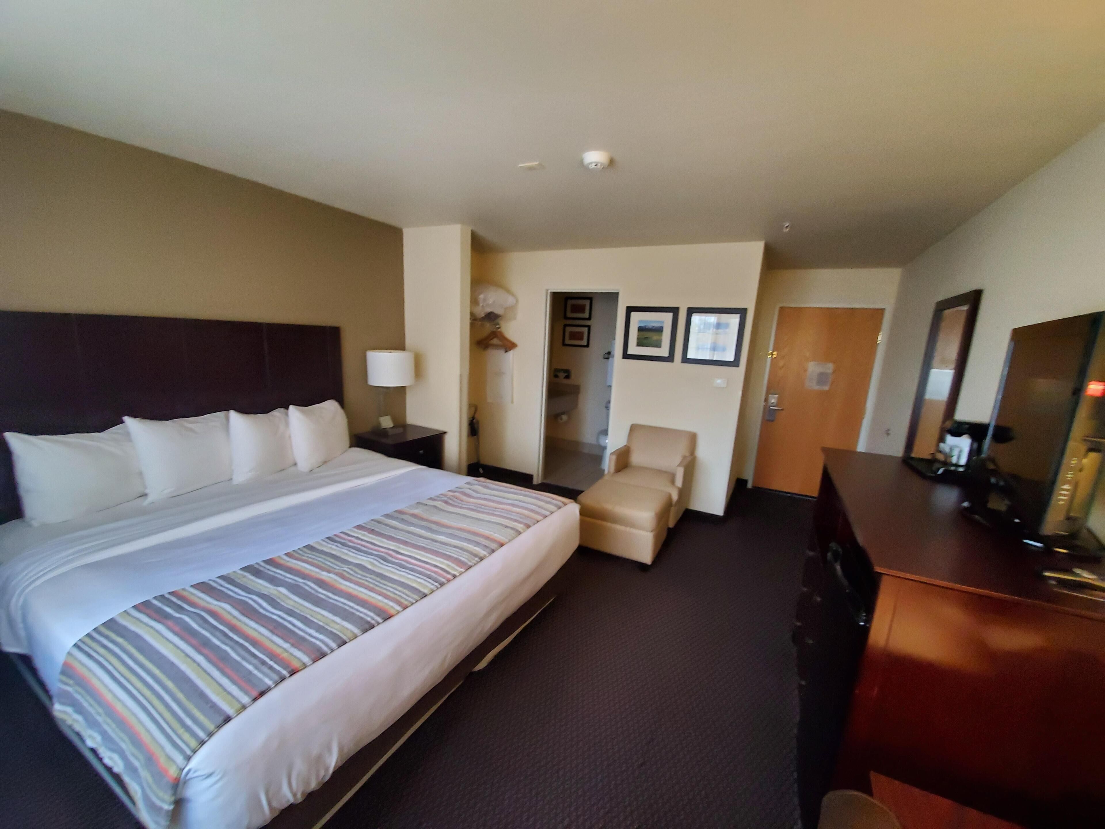 Una habitación de hotel con una cama grande, una silla, un aparador y una puerta que da a un baño.
