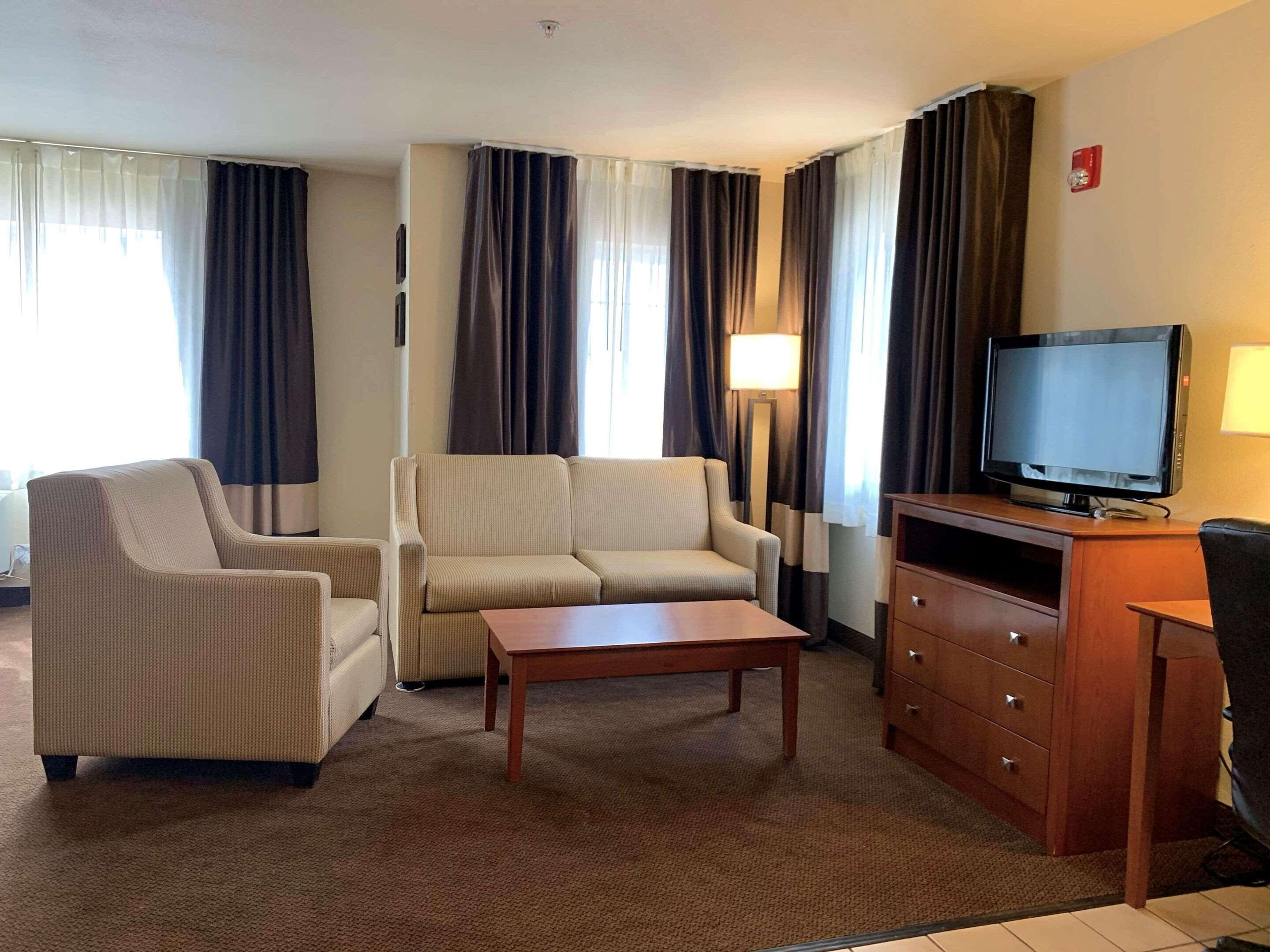 A hotel room with a sofa, armchair, TV, and a small table.