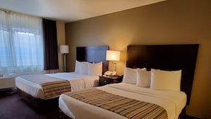 Una habitación de hotel con dos camas, una mesita de noche con lámpara y una ventana con cortinas.