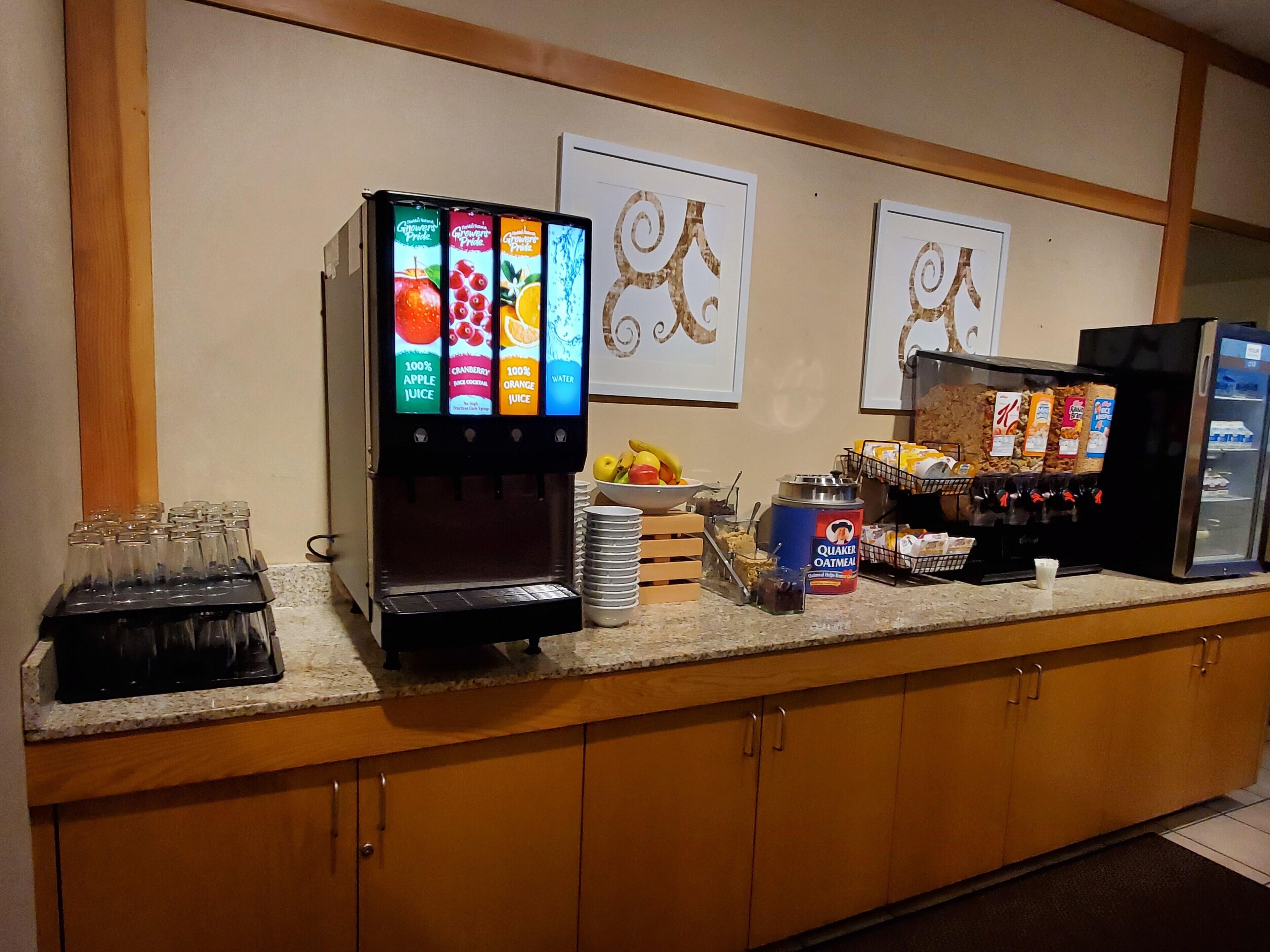 Un comptoir pour le petit-déjeuner avec un distributeur de jus, un bol de fruits et un paquet de flocons d’avoine Quaker.