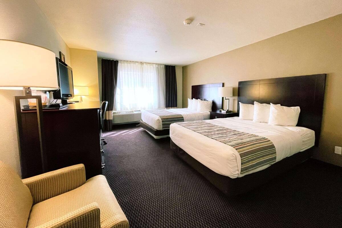 Habitación de hotel con dos camas, un escritorio, una silla y un televisor.