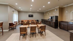 A spacious dining area with multiple tables and chairs, a kitchen area with dark cabinets, and a flat-screen TV mounted on the wall. - Best Western Plus Delta Inn & Suites (Oakley)