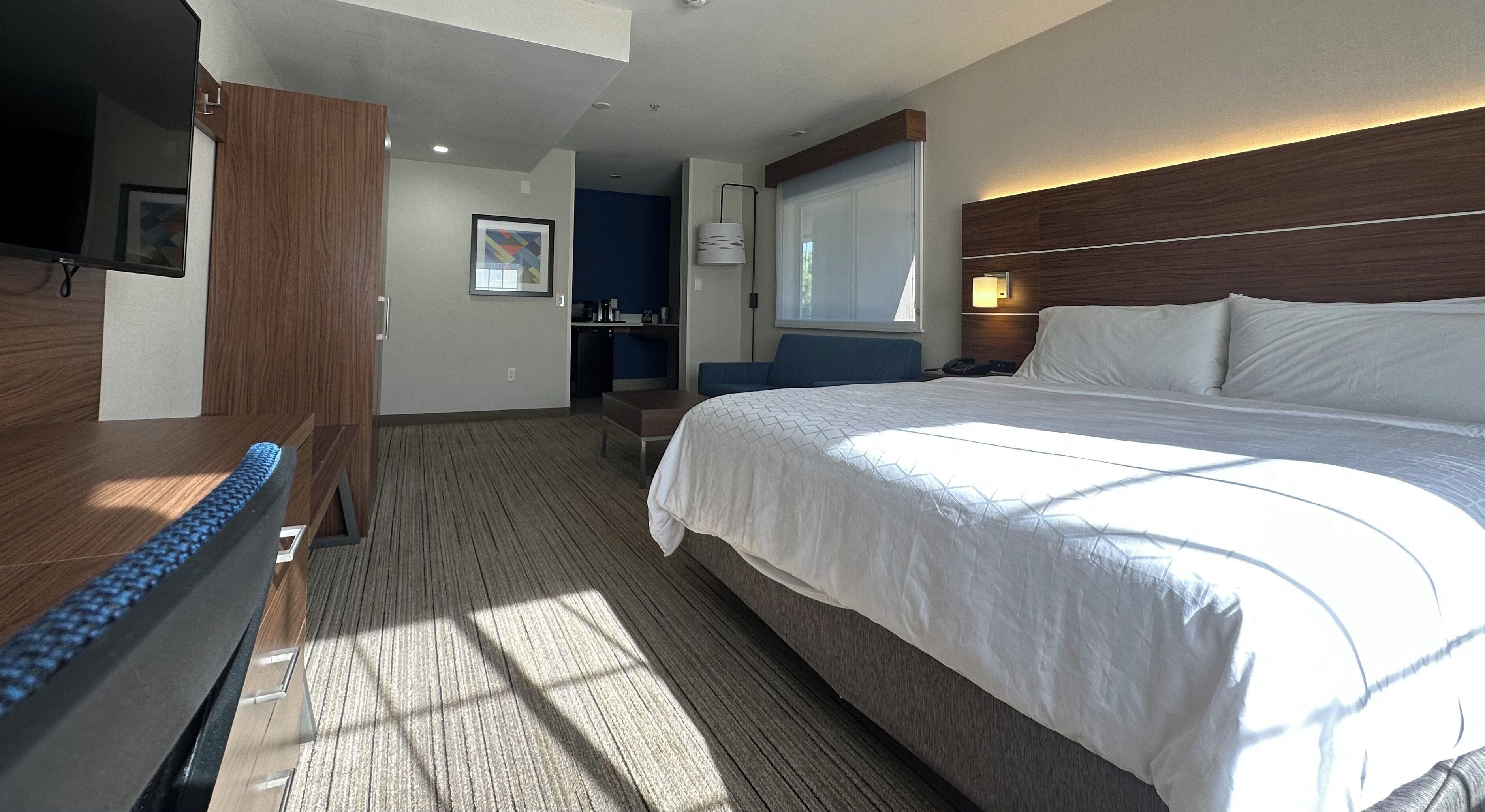 Een hotelkamer met een groot bed, een bureau, een stoel, een televisie en een raam met gordijnen.