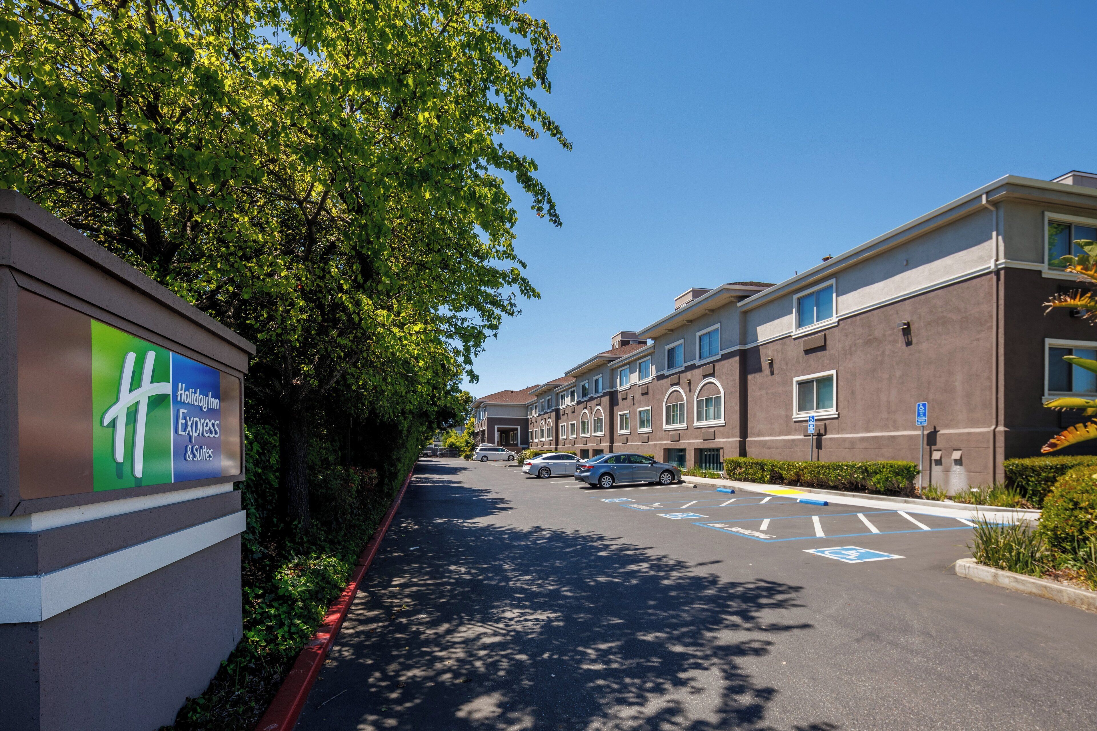 A parking lot with a Holiday Inn Express sign, a row of multi-story buildings, and a clear blue sky.